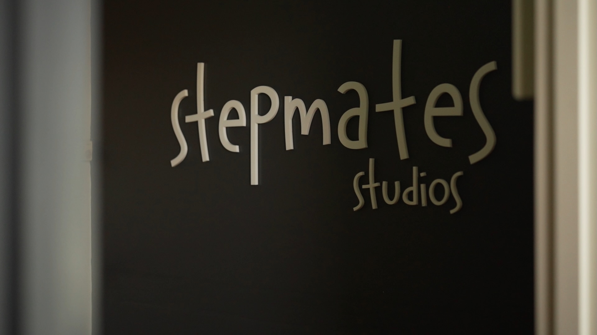 White letters that read "Stepmates Studios" affixed to a black wall seen through a doorway.