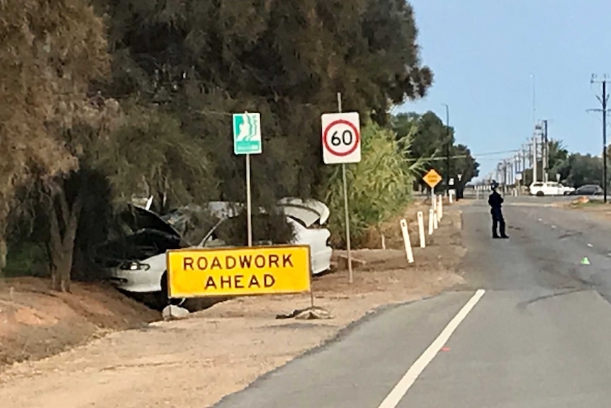 A white sedan crashed into a tree with a police officer standing beside it on the road