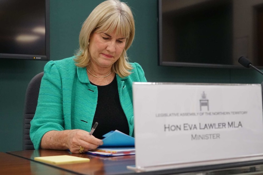 Eva Lawler sits  on a chair and looks down at a pile of papers lying on a desk.