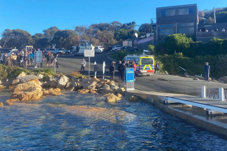 A crowd of people near a pontoon with an ambulance nearby