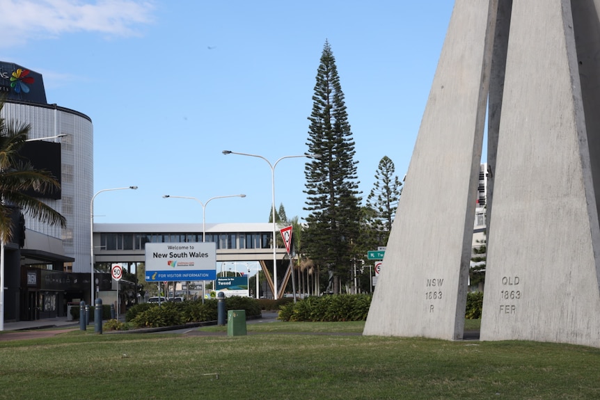 two triangular cement structures with QLD and NSW engraved in forefront, welcome to NSW sign behind