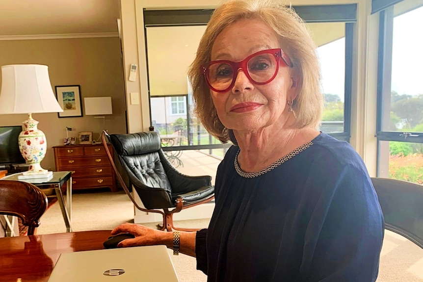 A woman wearing red glasses sits at a desk