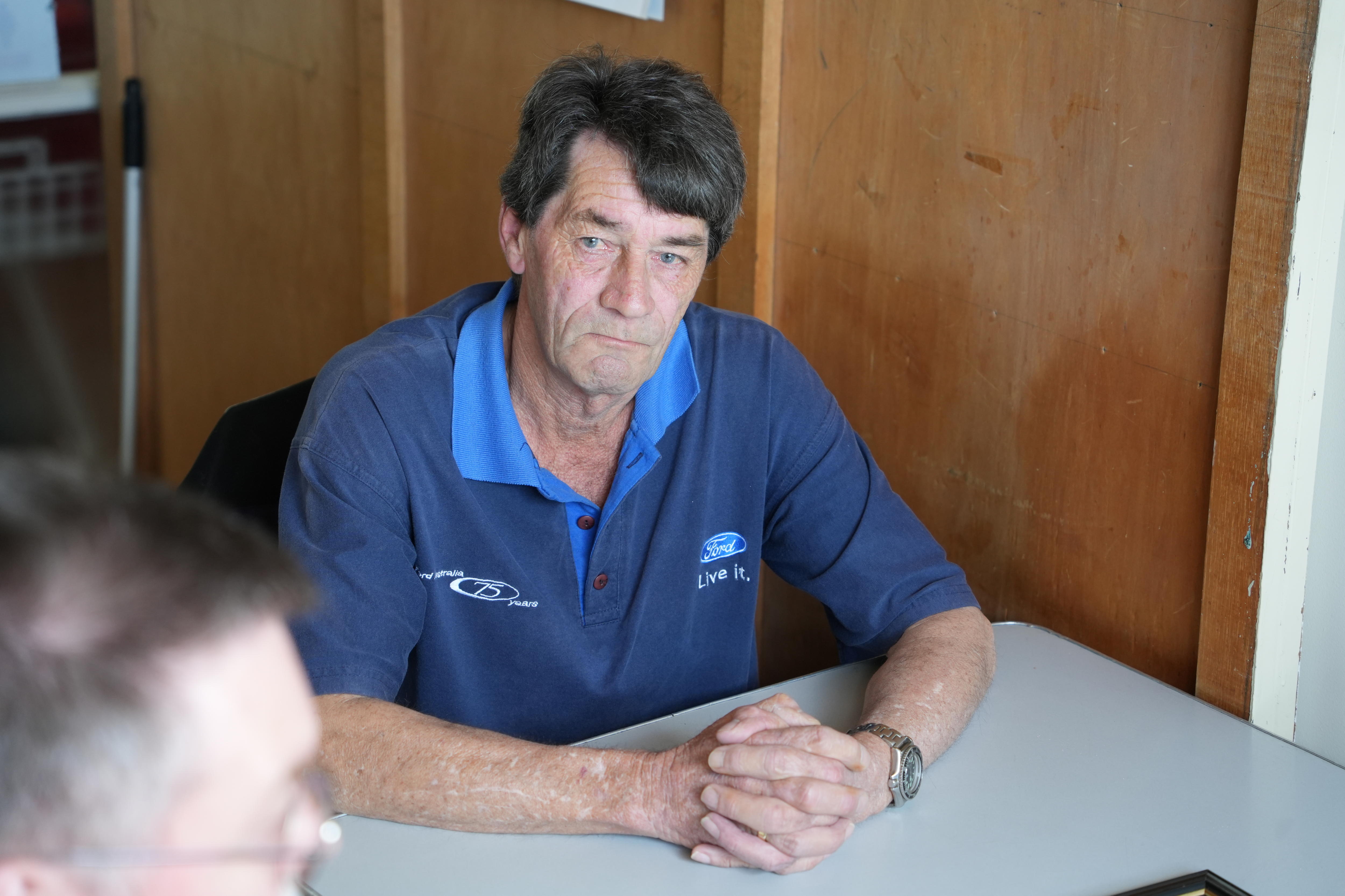 A man with black hair (Tony Travers) wearing a blue Ford polo T-shirt sitting at a table.