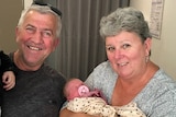 A man and a woman holding a newborn baby and smiling