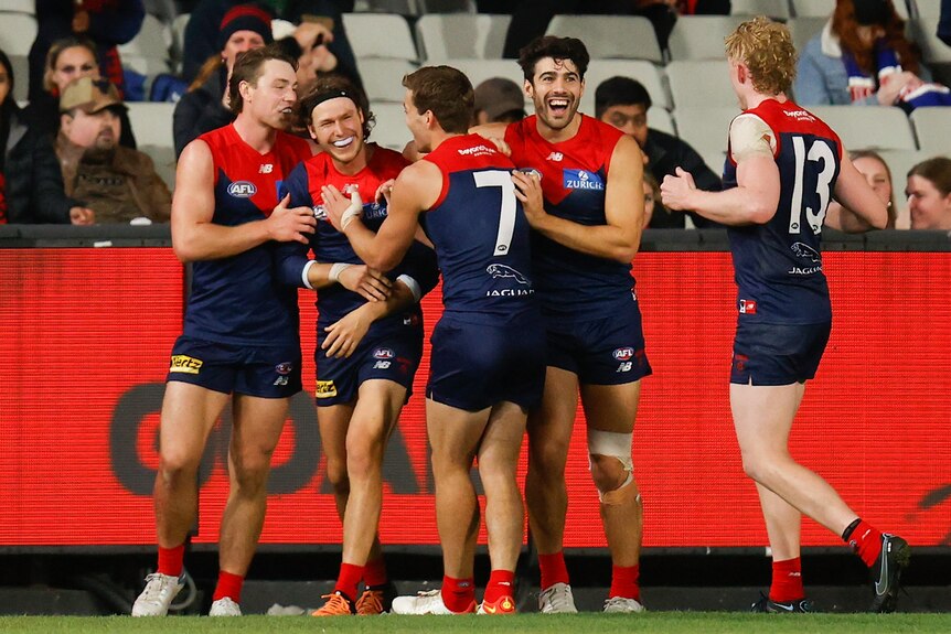 Christian Petracca and other Melbourne players smile while congratulating Ed Langdon