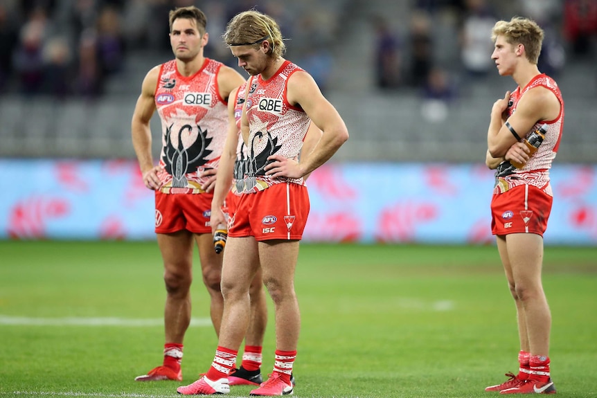 A group of Sydney Swans AFL players stand looking disappointed after losing to Fremantle.