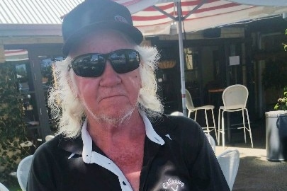 A man with long white hair, wearing a cap and sunglasses.