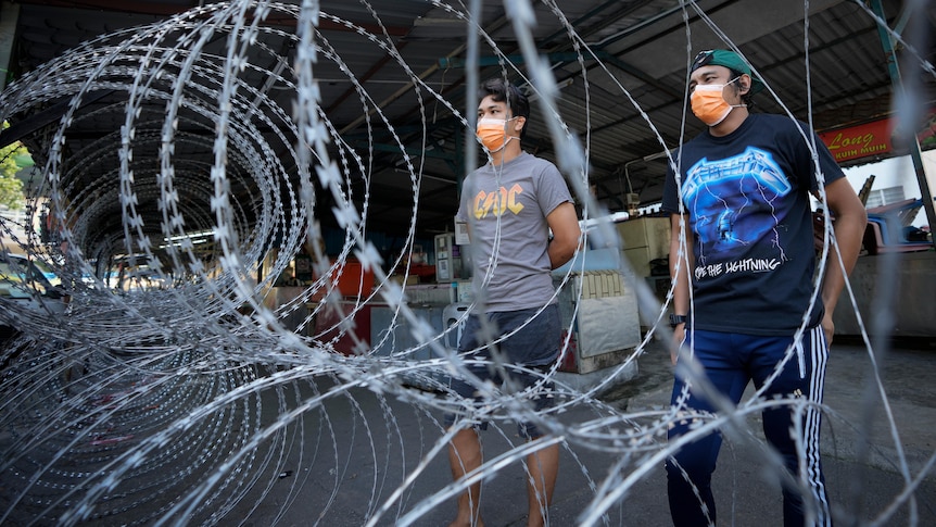 Residents wearing face masks stand behind barbwire in Malaysia