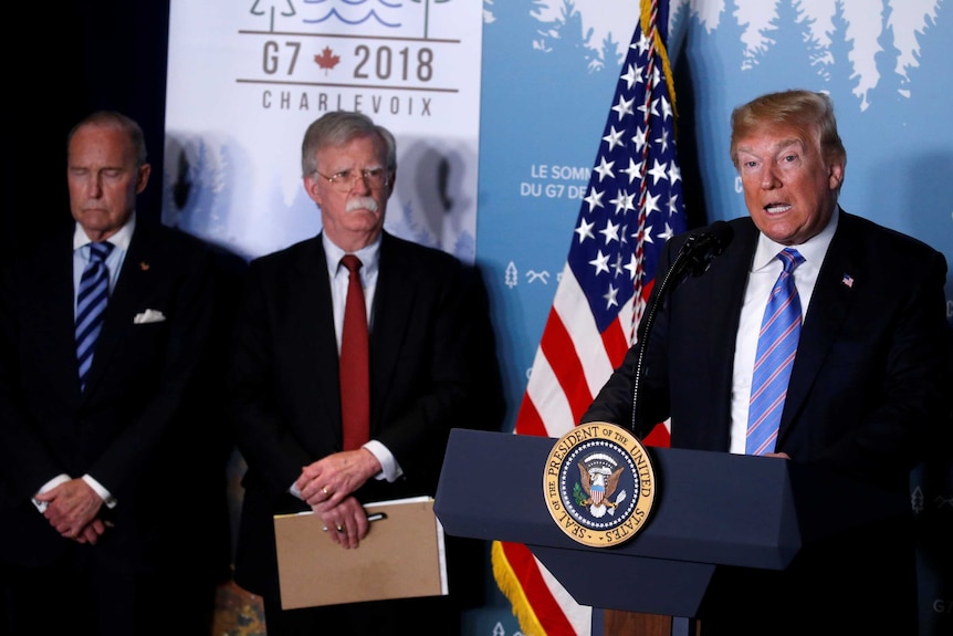 Donald Trump speaking at news conference at the G7 summit, standing next to John Bolton and Larry Kudlow.