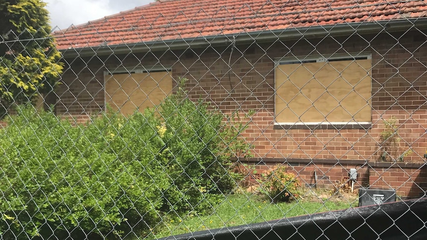 A boarded up brick building as seen through a wire fence.