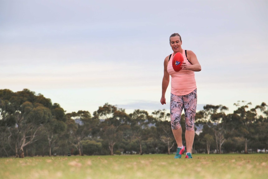 Lucy Finlay jogging on an oval with a football in her hands