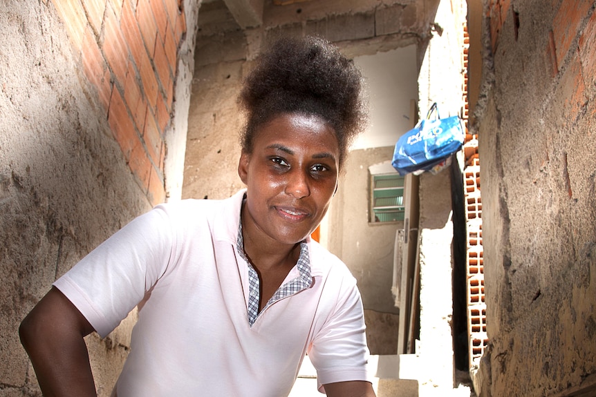 A woman crouches in an alleyway with a slight smile on her face