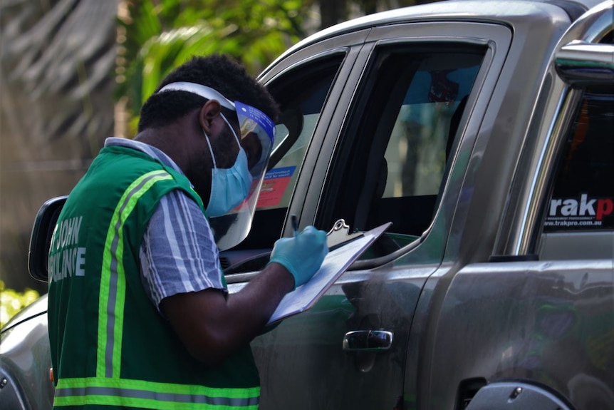 Healthcare worker fills in form on a clipboard at a drive-through testing clinic.