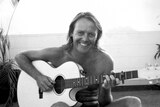 Black and white photograph of a man playing the guitar with long hair