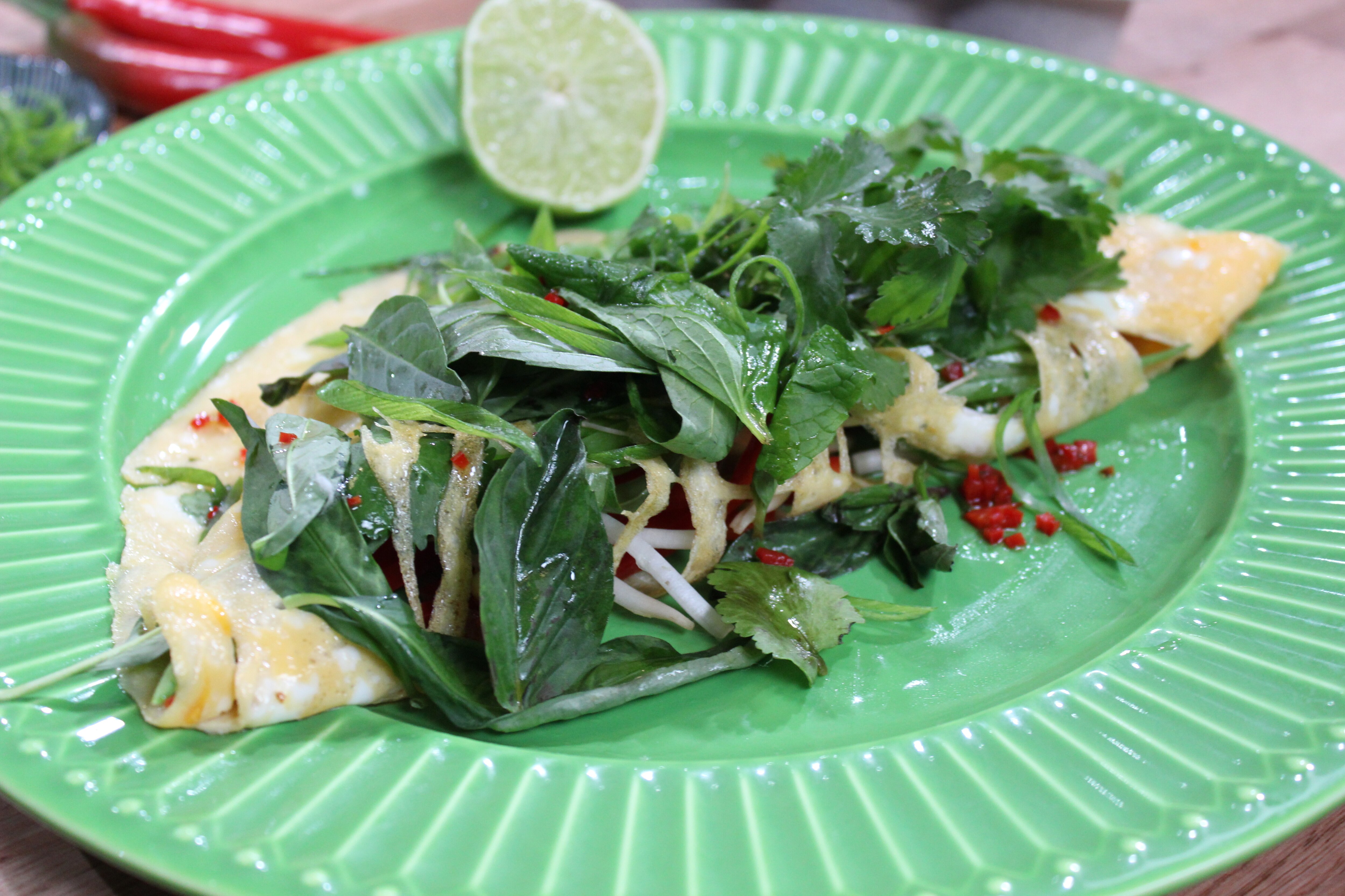 An omelette, topped with lots of green herbs, on a green plate with a lime next to it