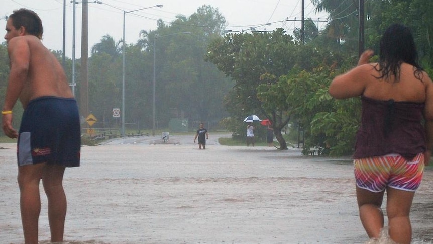 People stand in floodwater covering a road.