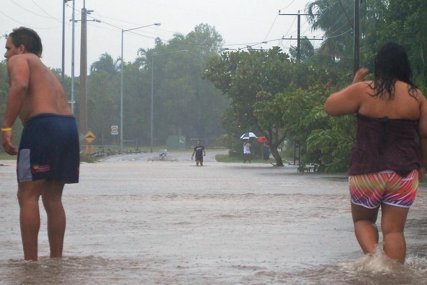 People stand in floodwater covering a road.