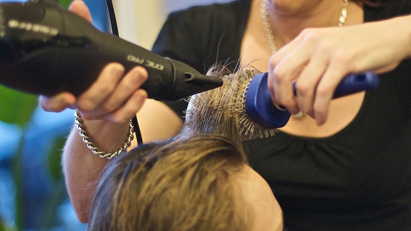 A hairdresser blow dries a customer's hair. Both faces are obscured.