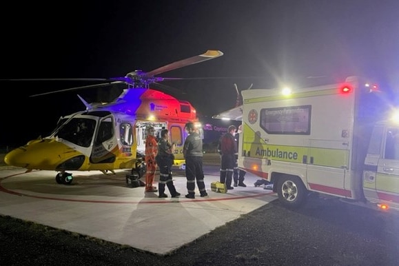 Paramedics stand near an ambulance and a rescue helicopter, speaking with each other.