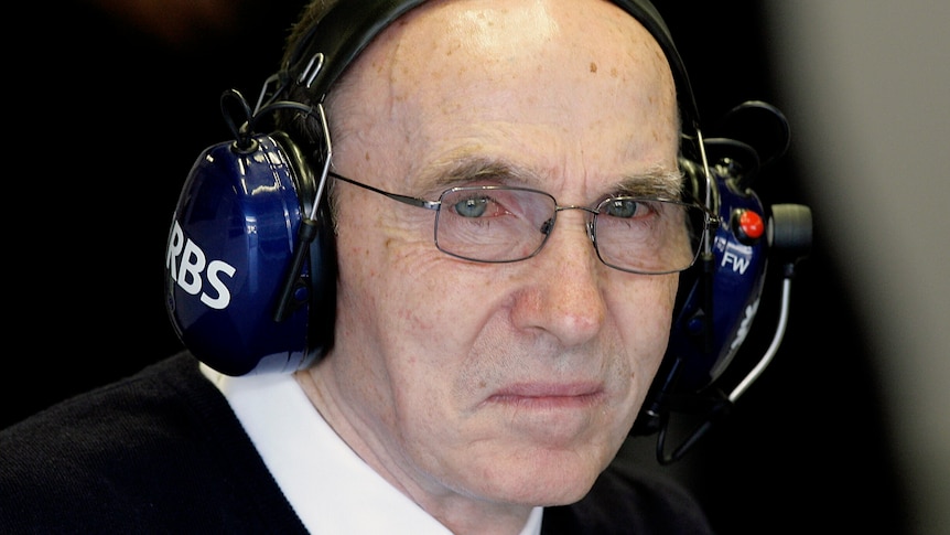 A Formula One team owner wearing glasses and a headset stares past the camera.