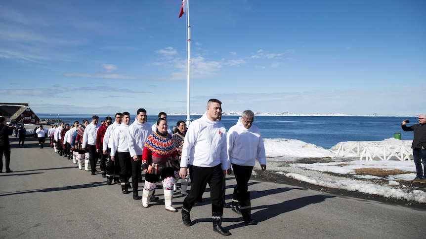 Greenland Prime Minister Kim Kielsen leads a group of people on a road alongside the ocean.