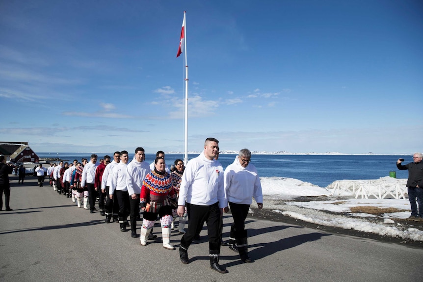 Greenland Prime Minister Kim Kielsen leads a group of people on a road alongside the ocean.