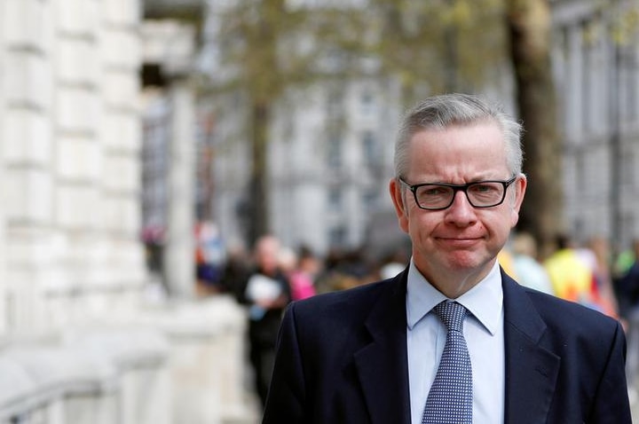 Michael Gove purses his lips as he looks straight ahead while walking on London street. He wears a suit.