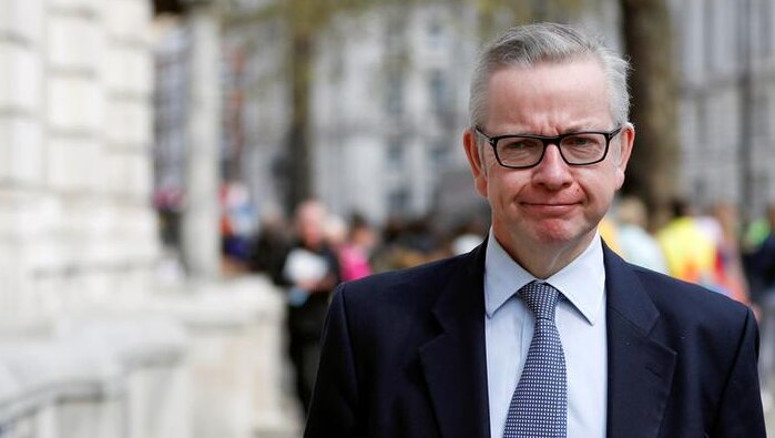 Michael Gove purses his lips as he looks straight ahead while walking on London street. He wears a suit.