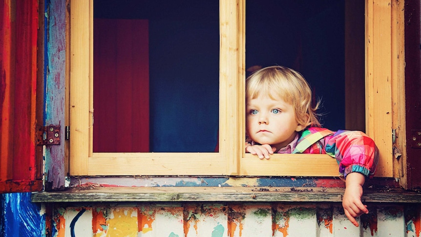 A small child with blue eyes looks forlornly out a window in a story about parenting only children during coronavirus pandemic.