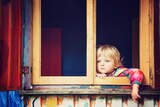 A small child with blue eyes looks forlornly out a window in a story about parenting only children during coronavirus pandemic.