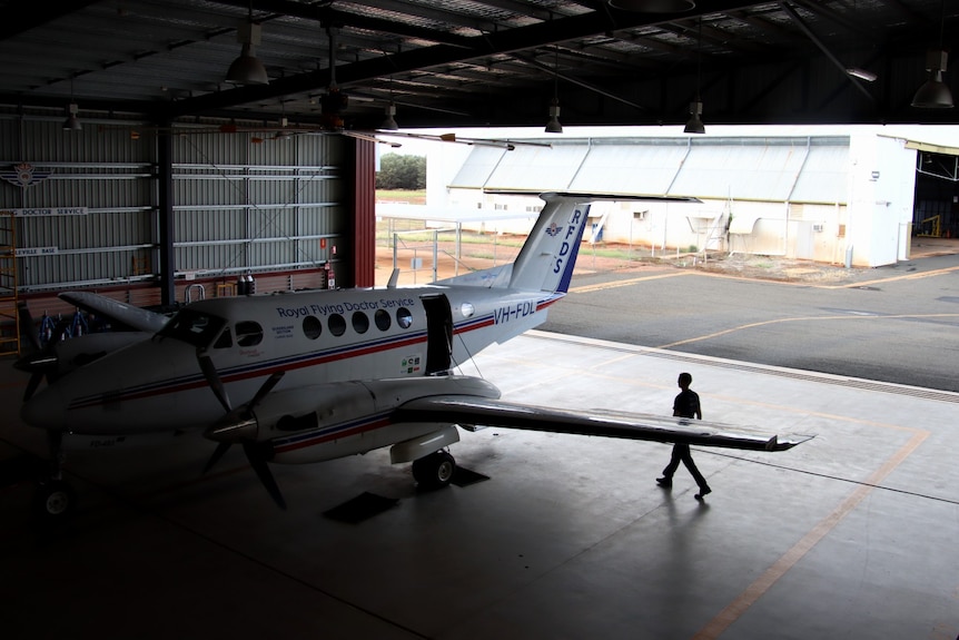 A silhouette of a man walks towards the rear door of a small plane in a hangar. 