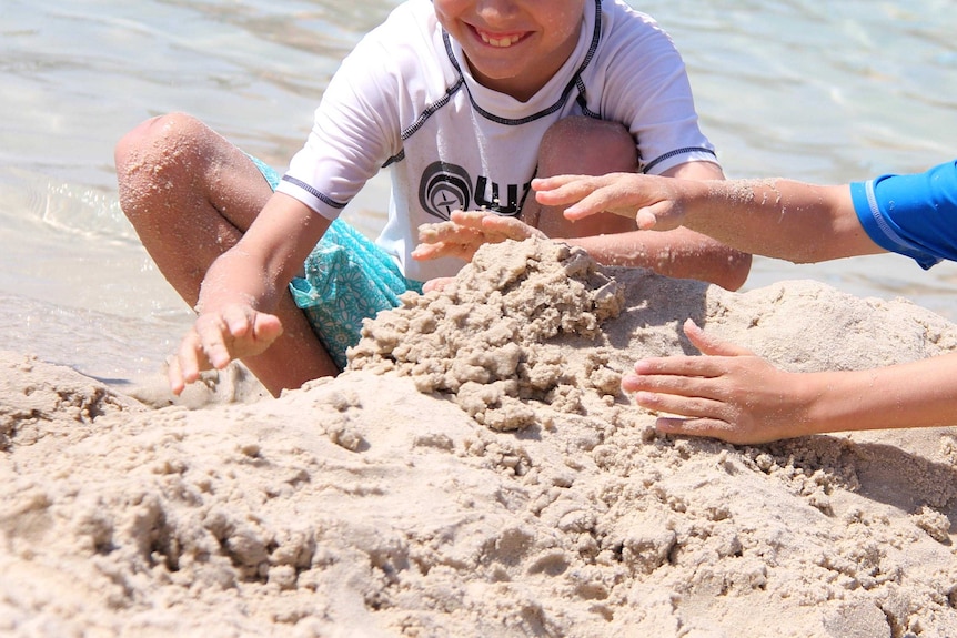 Two children play in the sand at the beach on a hot day.