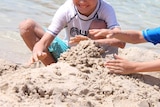 Two children play in the sand at the beach on a hot day.