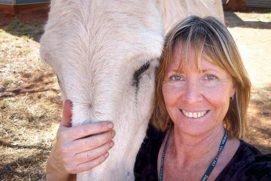 Health worker Gayle Woodford smiles as she poses for a photo with a horse