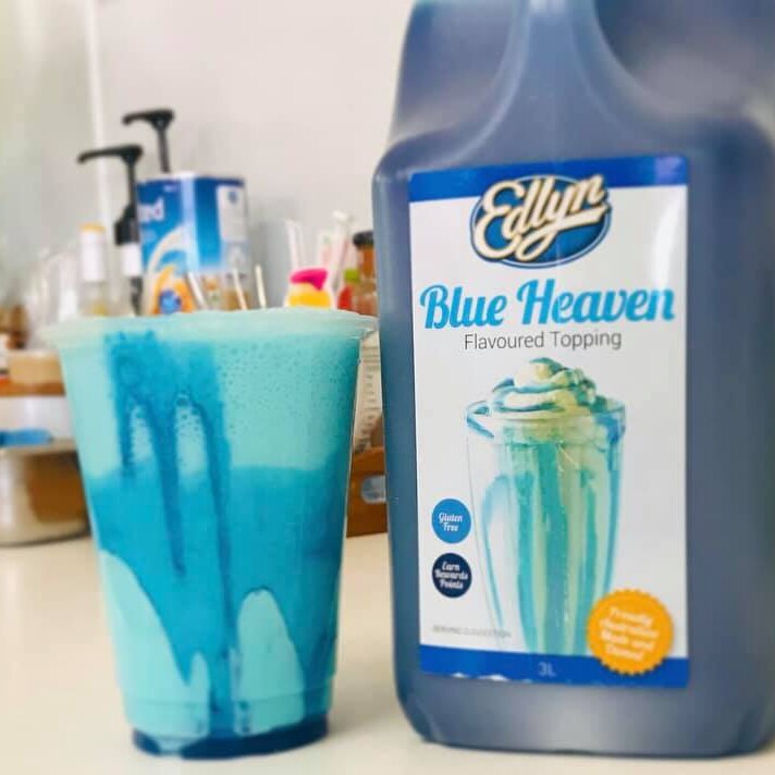 a blue milkshake in a glass alongside a plastic bottle of Blue Heaven flavoured topping