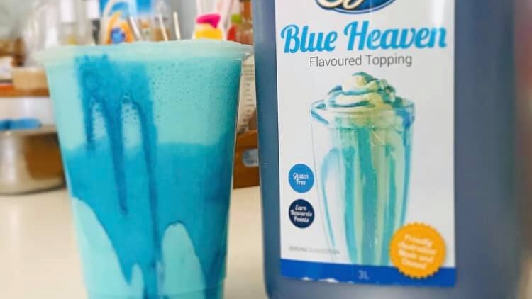 a blue milkshake in a glass alongside a plastic bottle of Blue Heaven flavoured topping