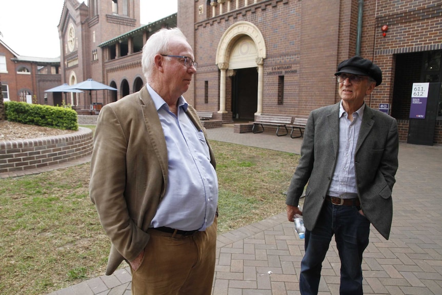 Two older men in suit jackets standing next to each other on the grounds of a school in Sydney.