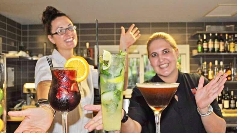 Two women behind a bar with three cocktails sitting on it