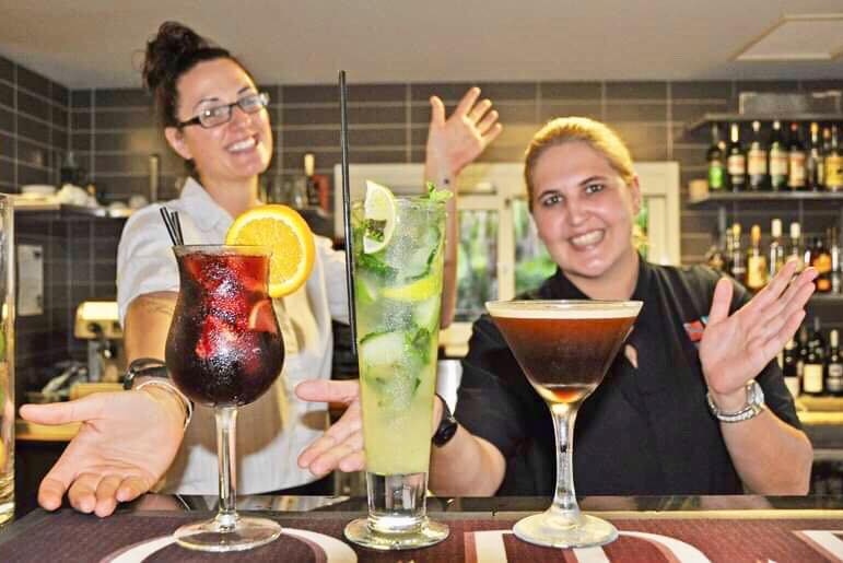 Two women behind a bar with three cocktails sitting on it