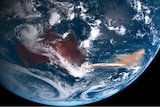 A satellite view of the Australian continent and a reddish plume flowing over the ocean from the east coast