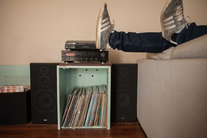 Feet in sneakers hang over the edge of a couch, near a record collection and turntable.