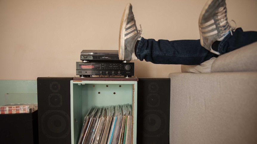 Feet in sneakers hang over the edge of a couch, near a record collection and turntable.