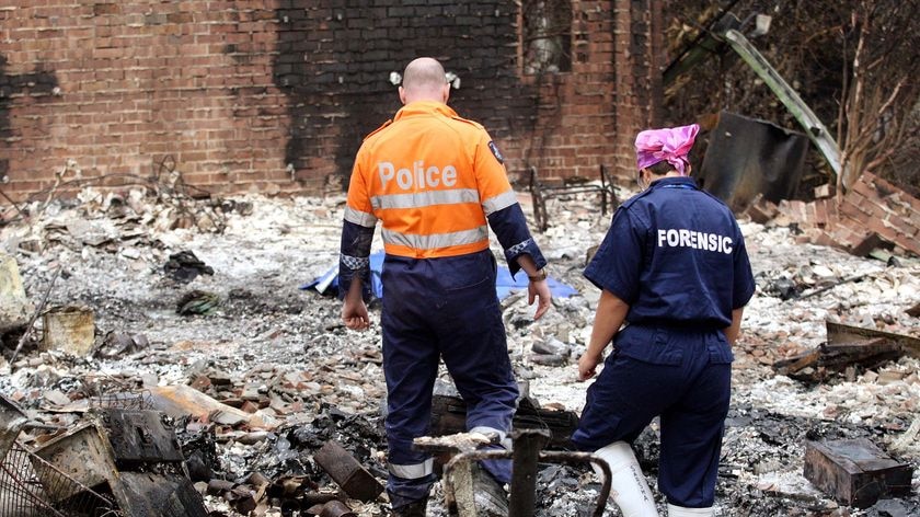 A policeman and forensics officer look over a house where five people died in a bushfire at Kinglake