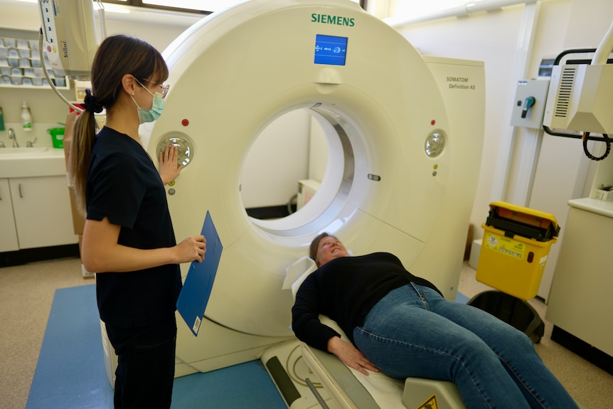 A woman lies on her back in front of an MRI scanner.