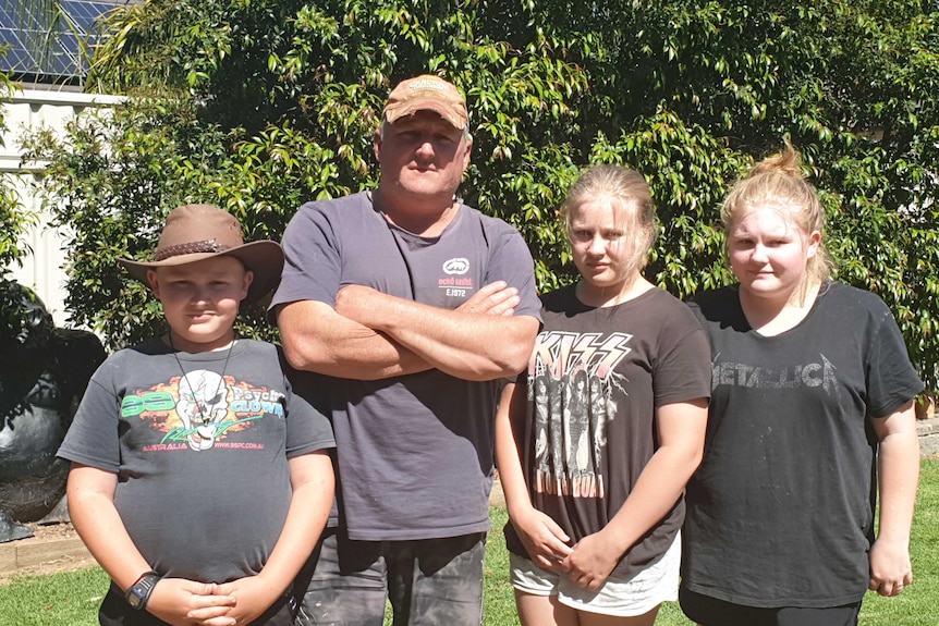 Craig Hope and his three children look at the camera in a backyard.