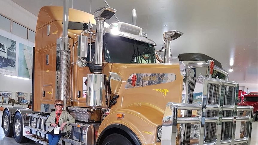 Maralyn standing next to a large bronze truck, indoors.
