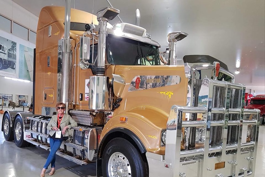 Maralyn standing next to a large bronze truck, indoors.