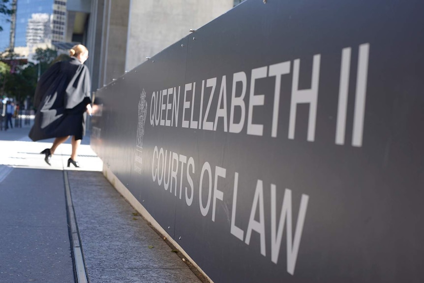 Sign outside Brisbane courts building with female barrister wearing silks walking into complex