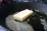 a small off-white rectangle sits in a pool of butter in a black frying pan
