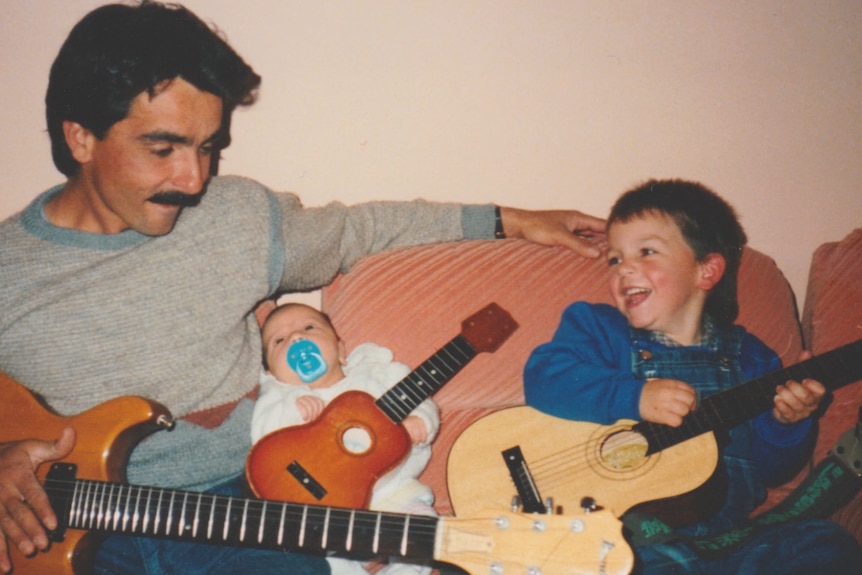 A photo of a man with young son and baby sitting on a couch